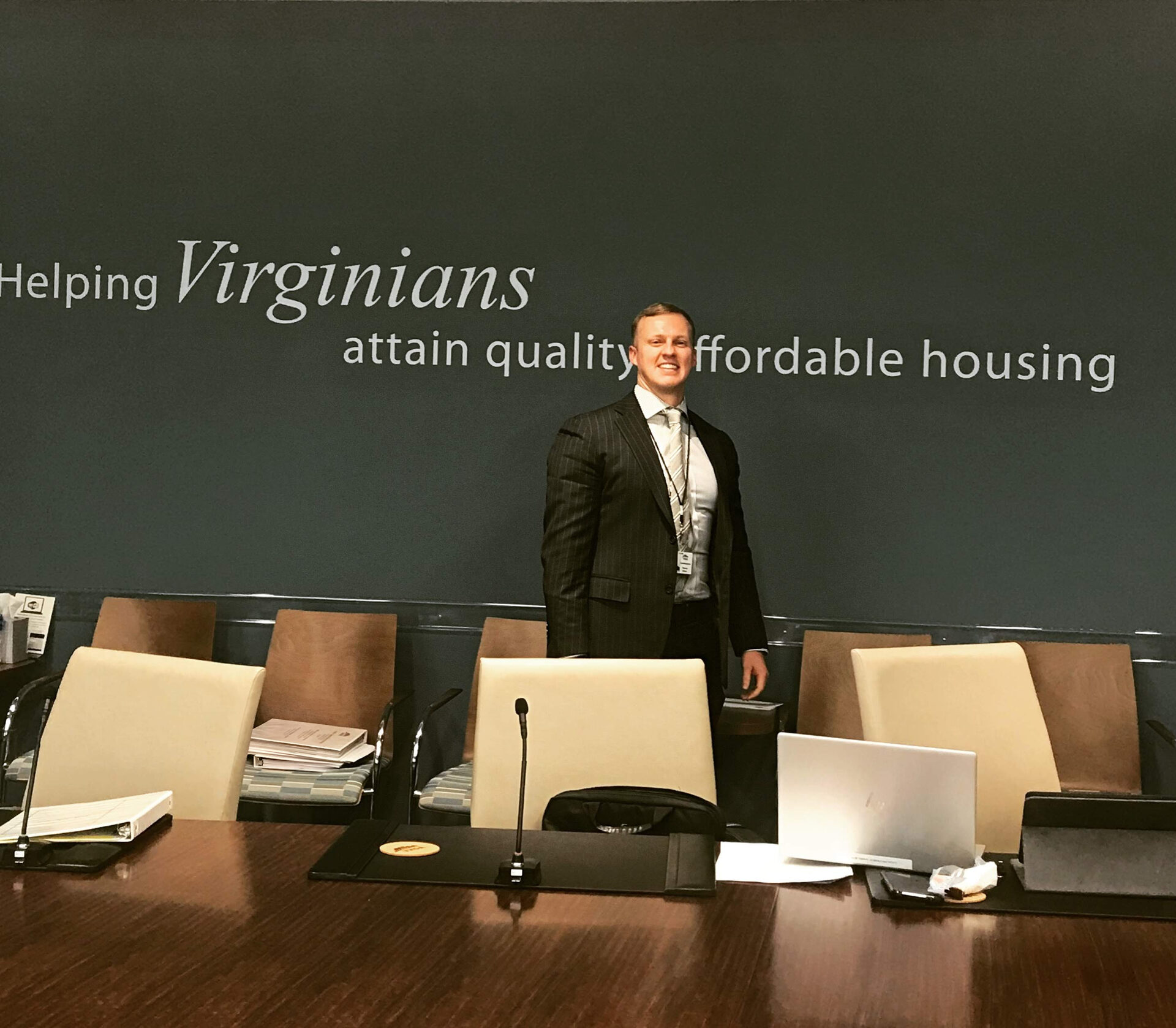 Thomas A. Gibson in the Virginia Housing boardroom, standing before a wall that reads “Helping Virginians attain quality affordable housing”